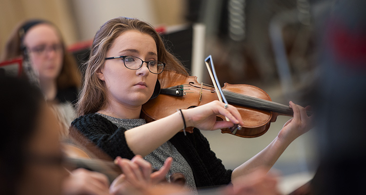 A student plays a violin in an orchestra rehearsal.