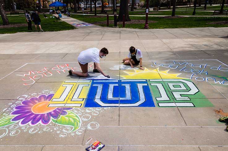 two students drawing the IUP logo in chalk on the walk