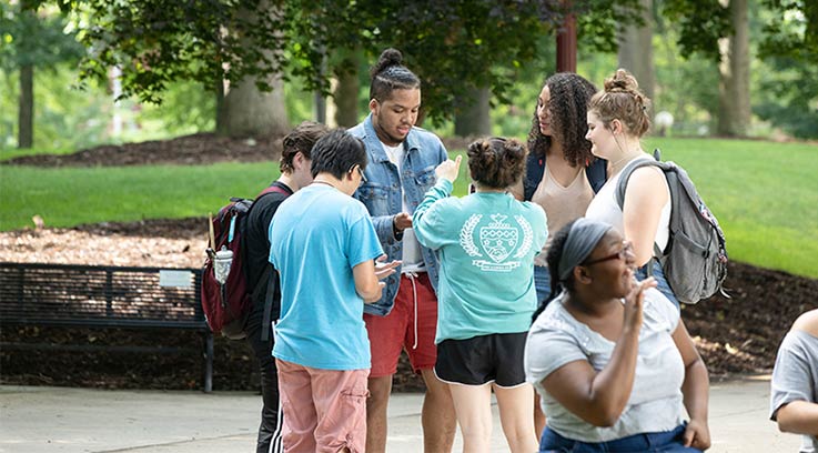 A group of students standing in a circle and talking in the Oak Grove