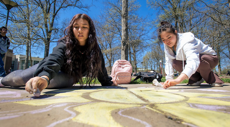 two students drawing on the sidewalk with chalk