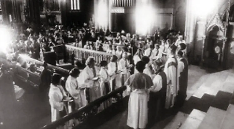 Black and white photo inside a church, with several people in robes standing for a ceremony