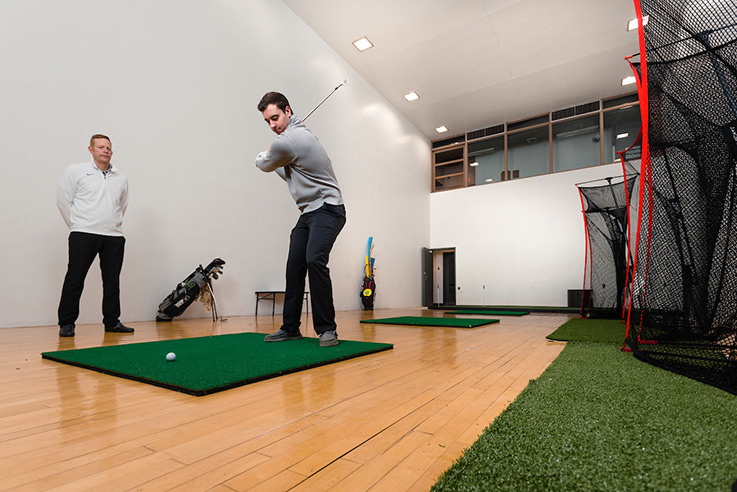 Dan Braun watches as golfer Jeremy Eckenrode practices his swing in the golf lab in the basement of Memorial Field House
