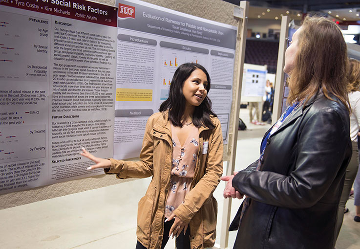 Research--Student discussing her poster with a woman at Scholars Forum. 