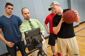 A Kinesiology professor instructs students from a laptop while one holds a basketball