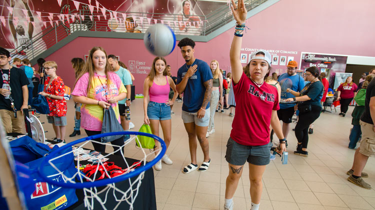 students gathered in the Kovalchick Complex at the carnival watching another throw a basketball in a game