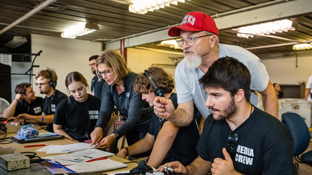 a group of student media students work in the studio under the guidance of their professor