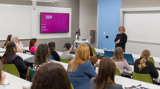 a faculty member leads a class of students seated at tables