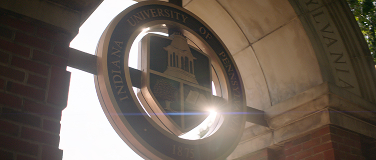 IUP emblem in a stone archway, lit by the sun