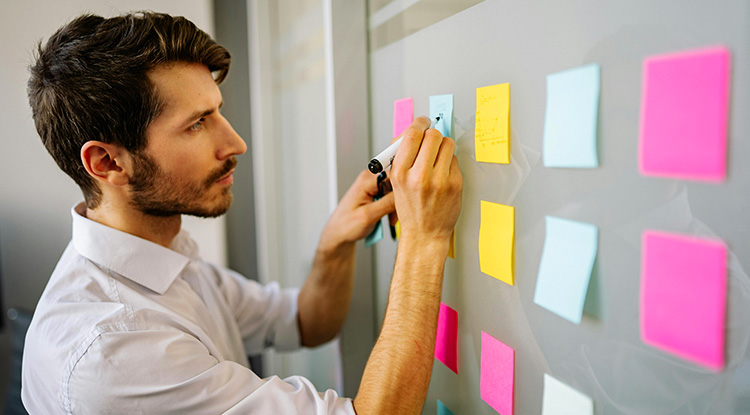 a man organizing colored post it notes on a white board