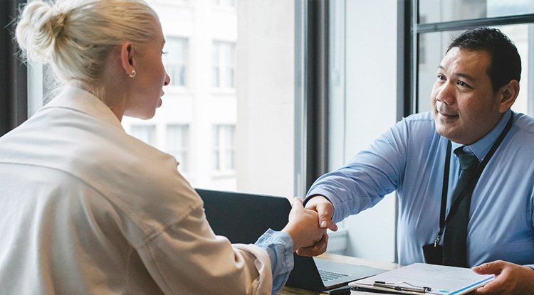 a man and woman sitting on each side of a desk shaking hands
