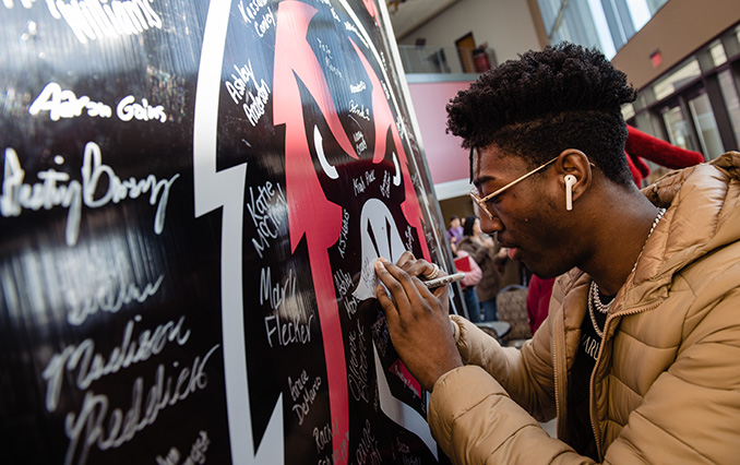 a new student signs their name next to a hawk logo