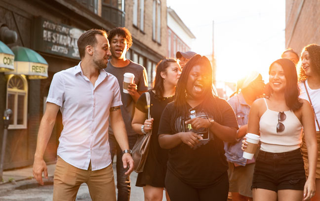 a group of students walking down a road laughing with one another while the sun shines on them from the background