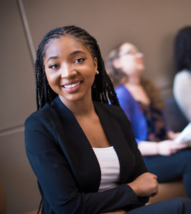 a young woman standing in a suit smiling at the camera while sitting at a desk