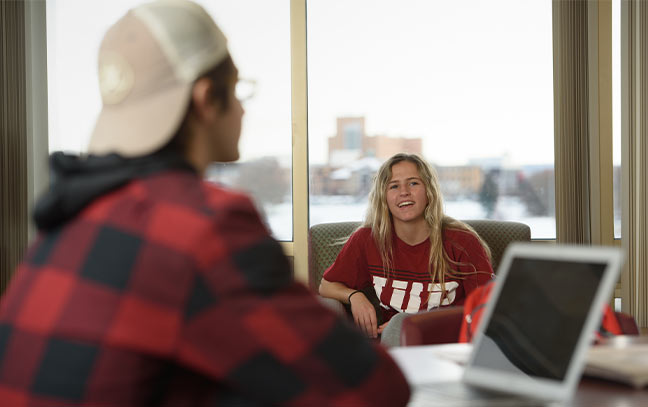 a female student smiles towards the camera while another is out of focus in the foreground