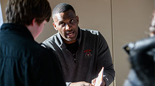 Two people sitting at a table talking. The person in the foreground is facing away from the camera.
