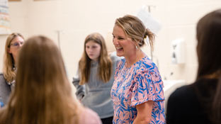 a woman in a pink and blue shirt stands smiling in a group of students