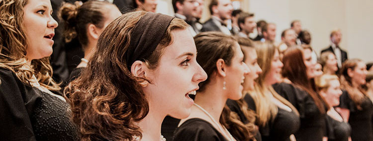 An image of a choir of mostly women singing on stage wearing black formal clothes