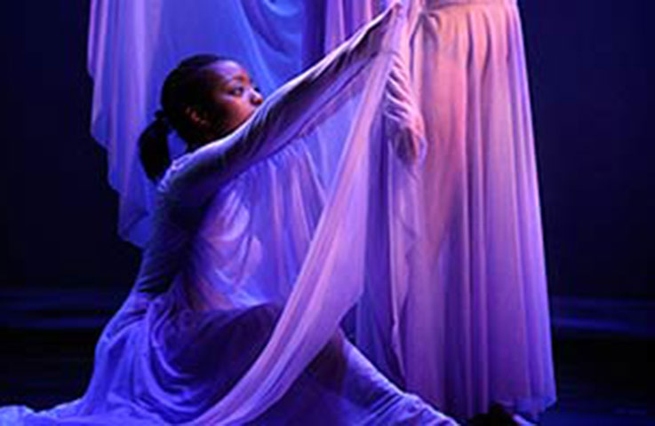 A female dancer in a flowing purple dress dances on a stage