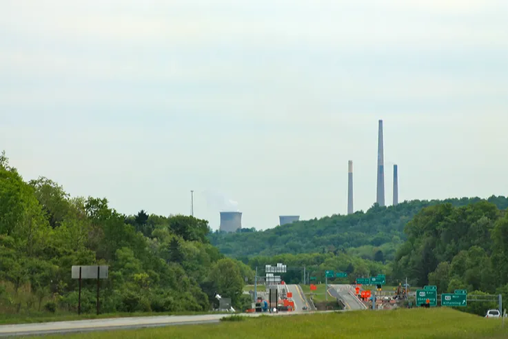 a highway going through the forested area with a power plant on the horizon