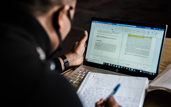 A student takes notes while studying with a laptop