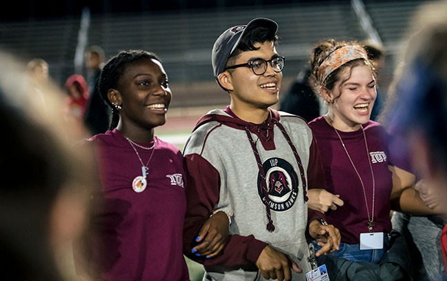 Three students link arms at a celebration