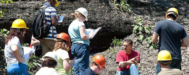 Students wearing hard hats take notes while working in the field 