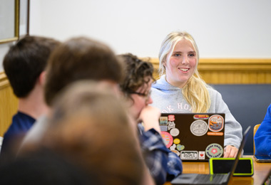 female student with an open laptop smiling in an honors classroom