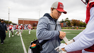 Athletic trainers kneel around an injured football player as cheerleaders stand in the background.