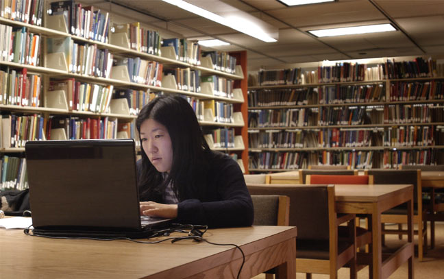 a student sitting at a desk in the library working on a laptop computer