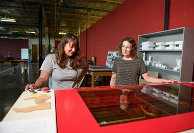 An student and Professor Sharon Massey use a large Rabbit Laser Cutter to cut matrix dies in the STEAM Shop.
