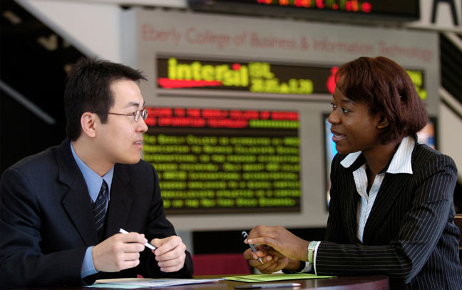 two people in business suits sitting at a table talking with one another