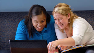 two students smiling while starting at a laptop computer screen