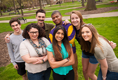 Group of diverse, smiling Honors college students standing in the Oak Grove.