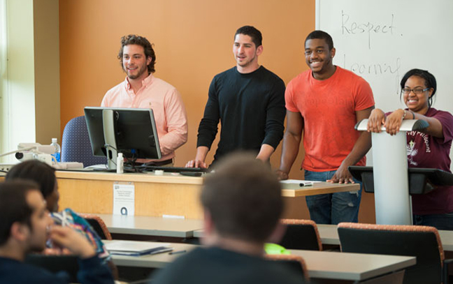 a group of four students stand presenting at the front of the classroom