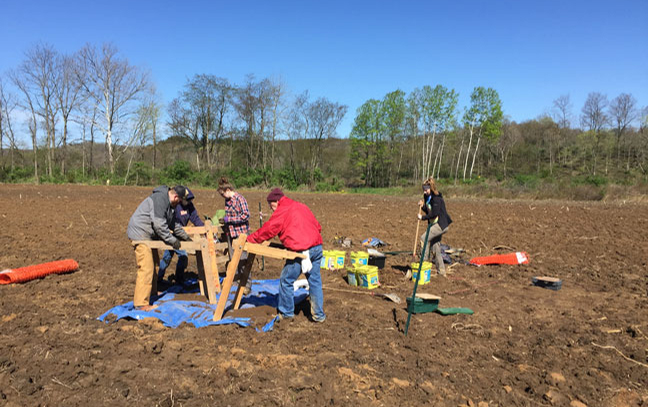 A group of five people building with wood pieces on a dirt field