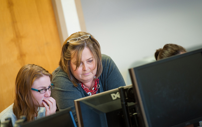 a teacher leans down to show a student something on their screen in a classroom