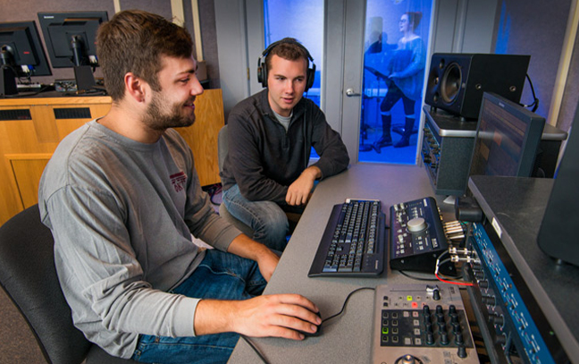 two males seated at a set of studio controls