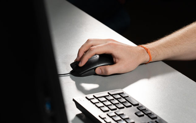 close up of a hand moving a computer mouse next to a keyboard