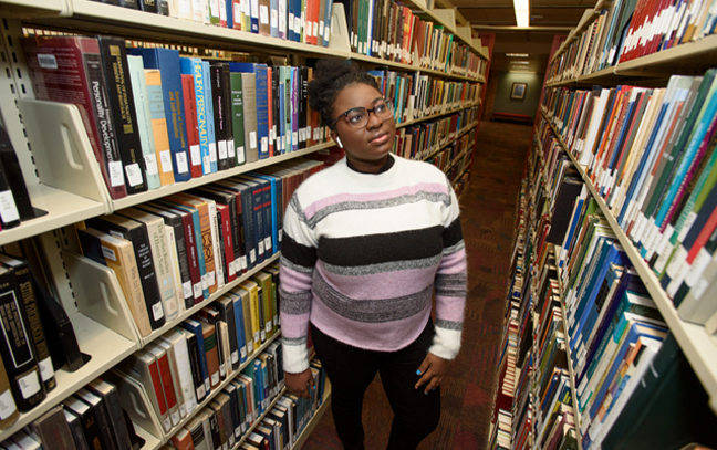 a female student walks through the stacks of books in a library