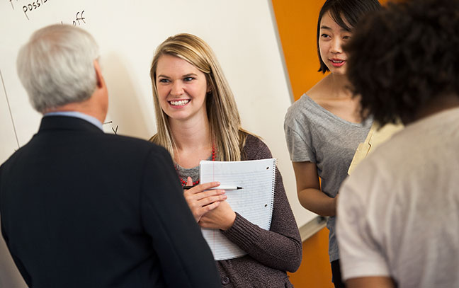 a female student stands talking to two professionals who have their backs to the camera