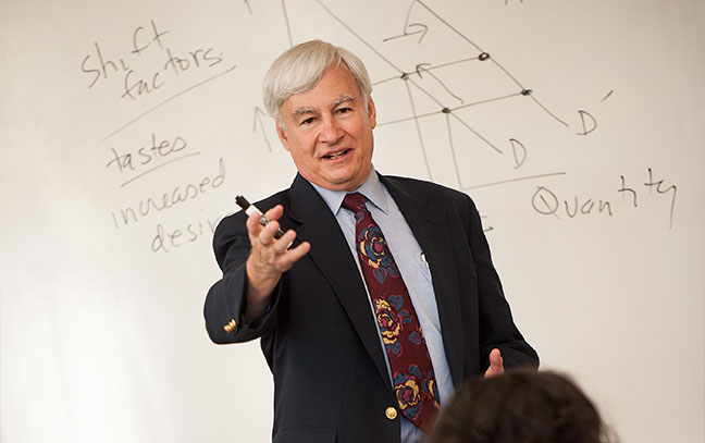 a professor teaching in front of a white board with formulas written on it