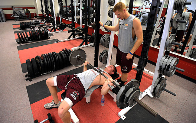 a person lifts weights while another spots them