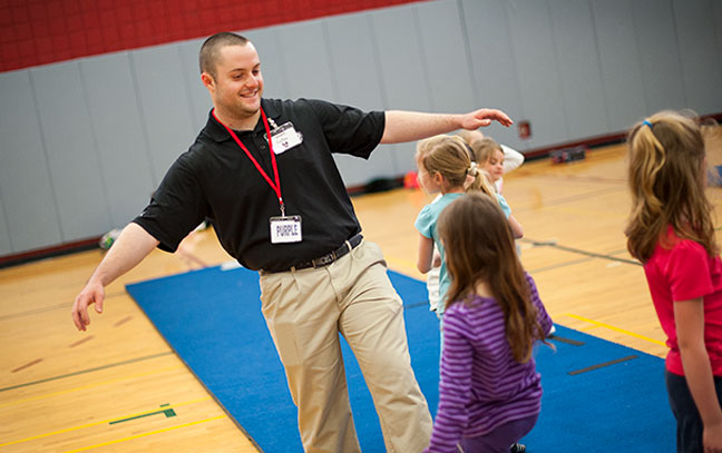 a student teacher leads a group of children in activities in a gym