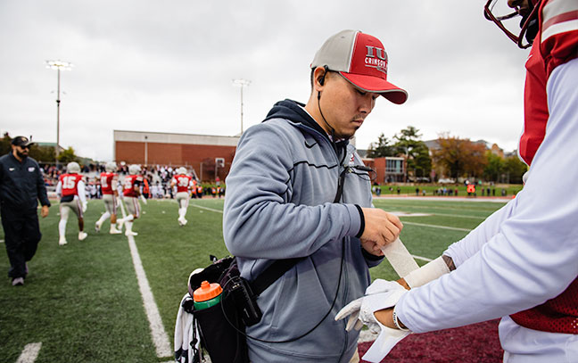an athletic training works with a football player on the field wrapping their arm