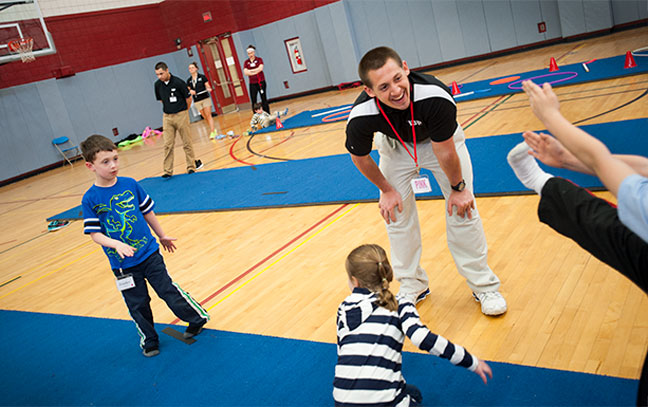 a male student teacher leans down to talk to small children during a class in a gym