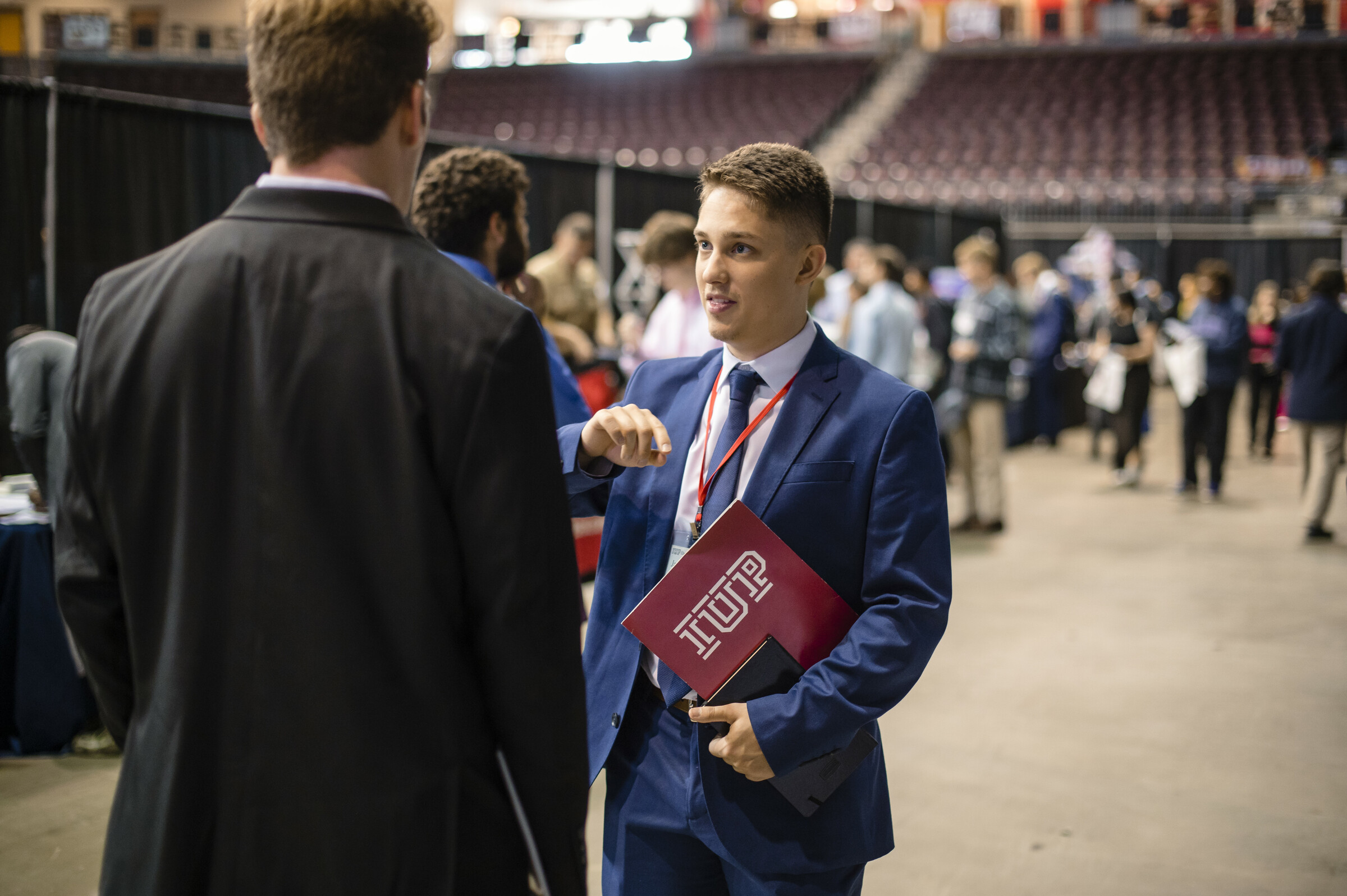 An IUP student in a suit and carrying a crimson IUP folder talks with a man at the Eberly Business Day event at IUP. 