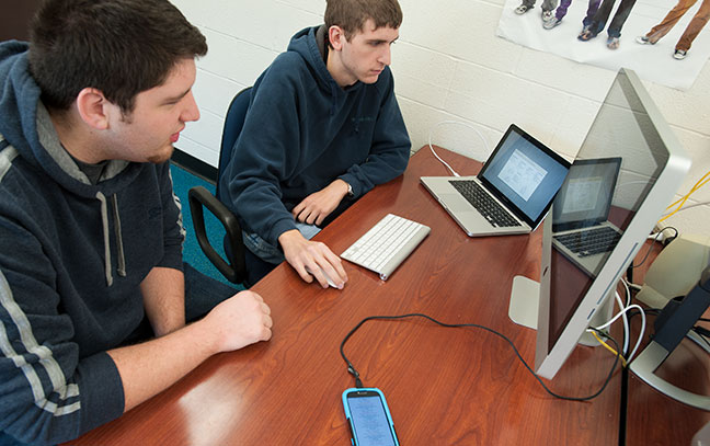 two male students look at a computer together