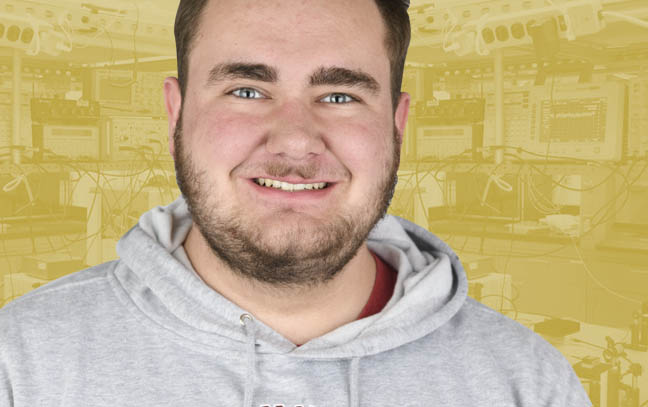 a male student in front of yellow backdrop with a bunch of technological equipment