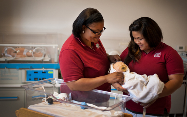 two nursing students in a simulation lab holding a simulation baby
