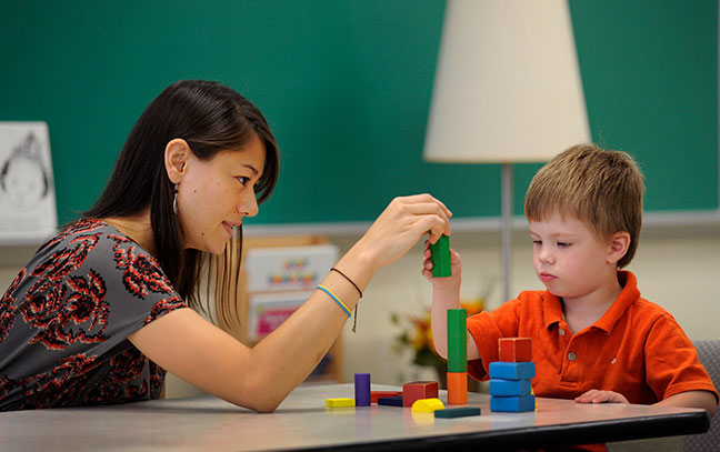 a female student teacher and a young boy play with blocks in a child care setting